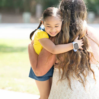 Datter krammer mor efter hun er kommet hjem fra skole med hendes smartwatch til børn fra Xplora med GPS tracking og trygge zoner.