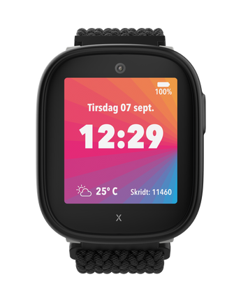 Xplora X6Play i sort med farverig startskærm, der viser tid, dato, vejr og skridttæller. Skærmen viser tirsdag den 7. september kl. 12:29.