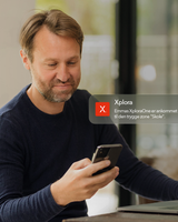 Forælder kigger på sin mobil derhjemme med en Xplora-notifikation om, at barnet er ankommet til en tryg zone.