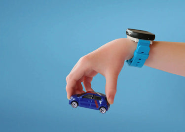Barns hånd med et Xplora smartwatch til børn på håndleddet leger med en blå bil