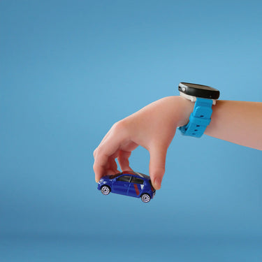 En barnehånd med et blåt smartwatch holder en lille blå legetøjsbil mod en solid lyseblå baggrund. Smartwatchet har en sort rektangulær skærm og en lys blå rem, der står i kontrast til barnets lyse hud.